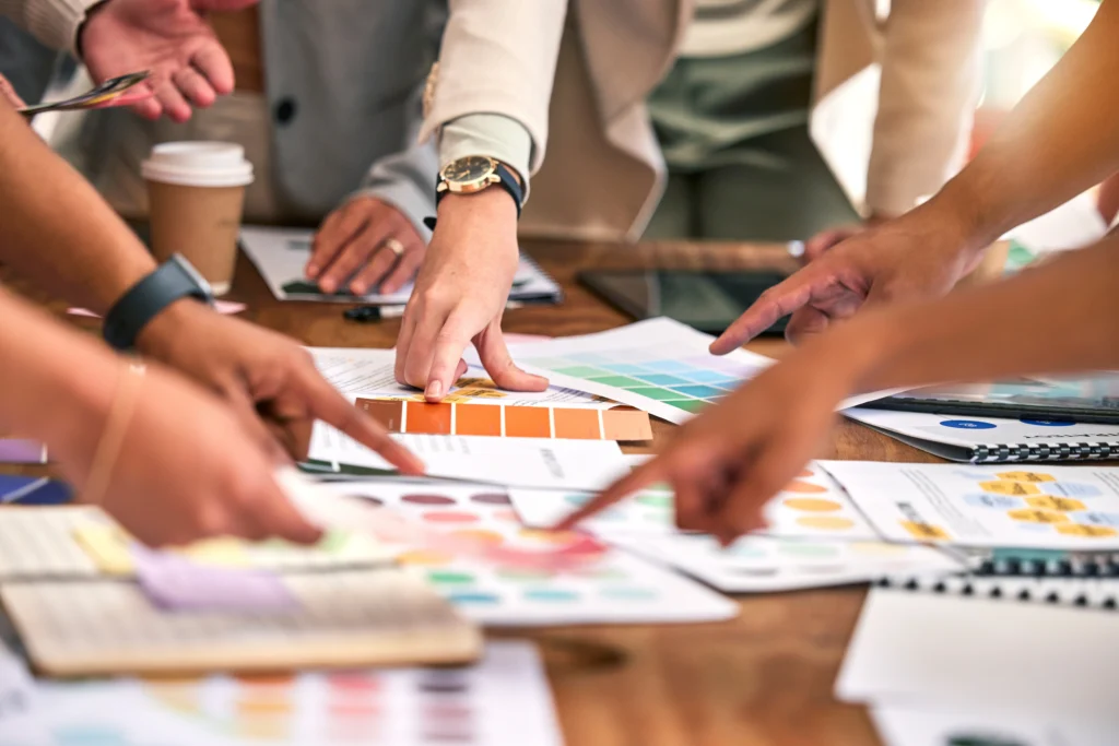 Réunion créative d'une équipe d'agence de communication autour d'une table, en pleine réflexion et collaboration pour définit l'identité visuelle et la direction artistique d'un client, avec croquis, couleurs et supports de branding.