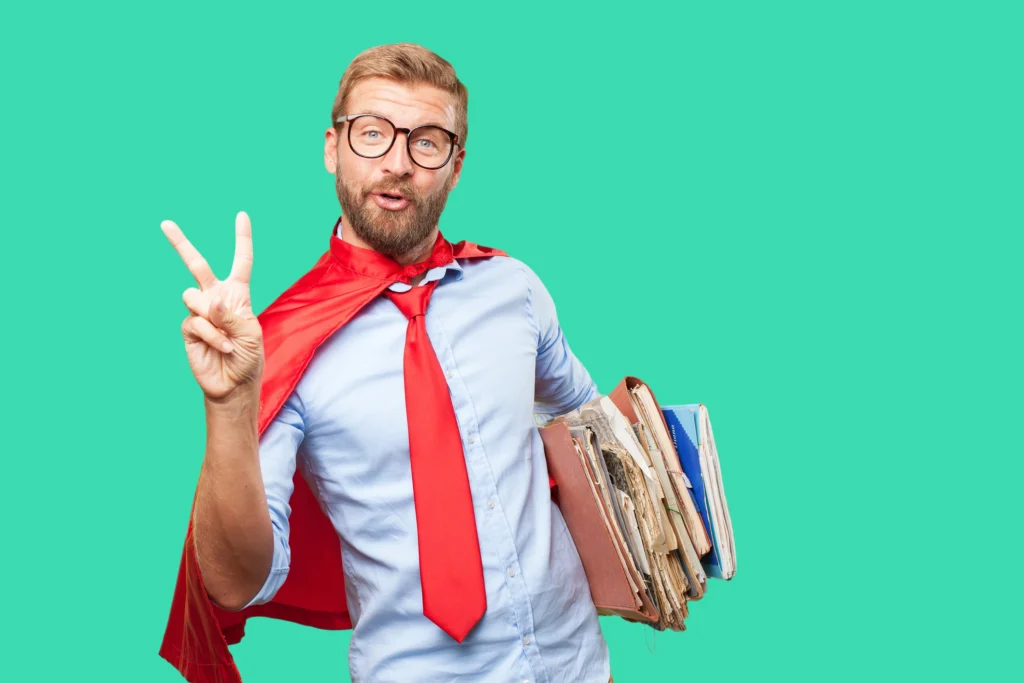 Photo humoristique d'un chef d'entreprise avec une cape de super héro, une cravate et des dossiers sous le bras en besoin un signe avec la main pour montrer l'importance de ne pas avoir besoin d'être un super héros ou une star des réseaux sociaux pour soigner son personal branding, mais de rester simple et authentique.