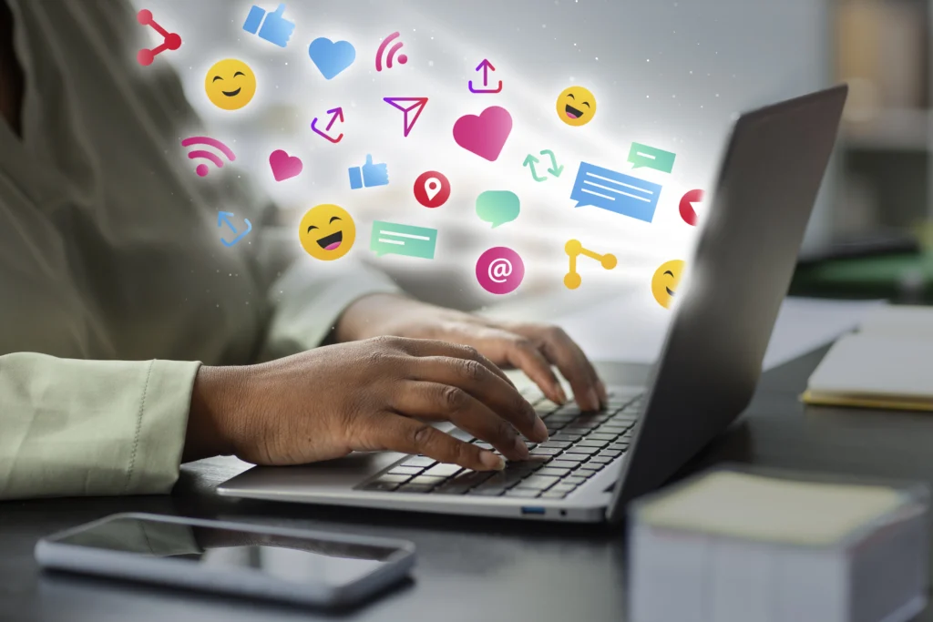 community manager devant son ordinateur portable en train d'animer et de gérer les réseaux sociaux d'une entreprise, avec pleins d'emoji et notifications devant l'écran pour illustrer l'importance et le travail du community management