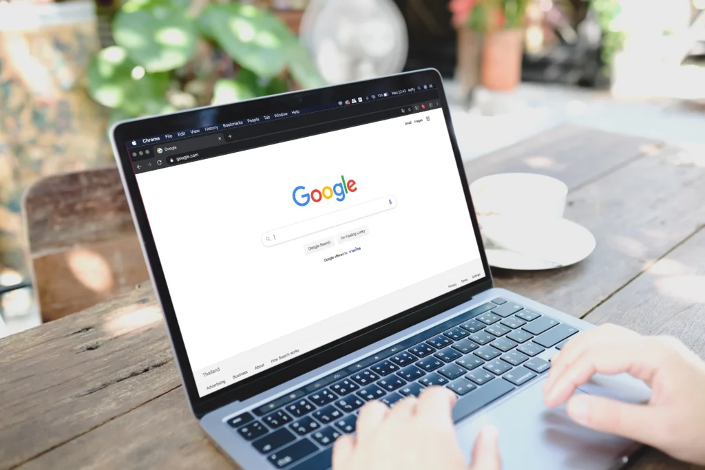 Main d'une personne prête à taper sur le clavier de son ordinateur portable pour effectuer une recherche sur Google, montrant l'importance d'avoir un bon référencement naturel (SEO) pour être facilement retrouvé sur les moteurs de recherches quand quelqu'un effectue une recherche
